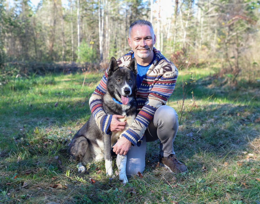 Dr Mark Roberts kneeling next to Husky mix dog, in the bush.