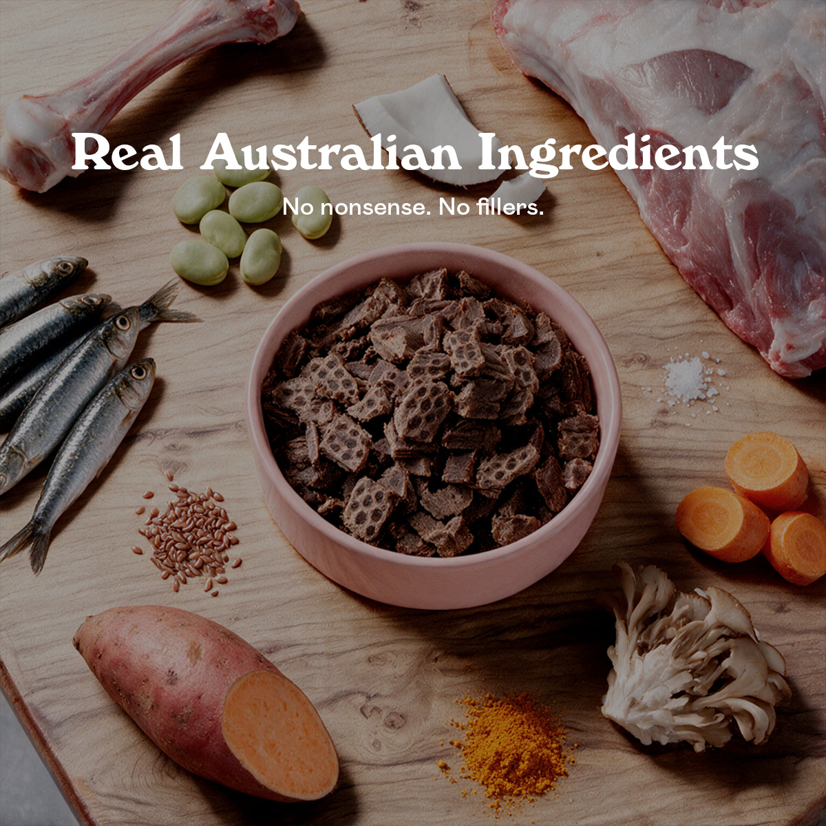 Pink bowl of Eureka Pet Co air-dried dog food surrounded by raw ingredients on a wooden board, including a lamb bone, sardines, broad beans, carrots, sweet potato, turmeric, flaxseed and mushrooms. Text reads Real Australian Ingredients, no nonsense, no fillers.