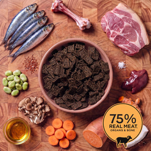 Pink bowl of Eureka Pet Co air-dried dog food surrounded by raw ingredients on a wooden board, including a lamb bone, lamb shoulder, sardines, broad beans, coconut, flaxseed, sweet potato, turmeric and carrots. Badge reads 75% real meat, organs and bone