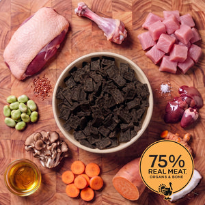 Cream bowl of Eureka Pet Co air-dried dog food surrounded by raw ingredients on a wooden board, including a bone, diced turkey, duck breast, broad beans, coconut, flaxseed, sweet potato, turmeric and carrots. Badge reads 75% real meat, organs and bone.